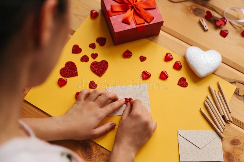 The girl wrote a letter with congratulations and pastes the envelope with a symbol in the form of a heart. Nearby lie. Various objects symbolizing the event royalty free stock photos The girl wrote a letter with congratulations and pastes the envelope with a symbol in the form of a heart. Nearby lie. Various objects symbolizing the event royalty free stock photos