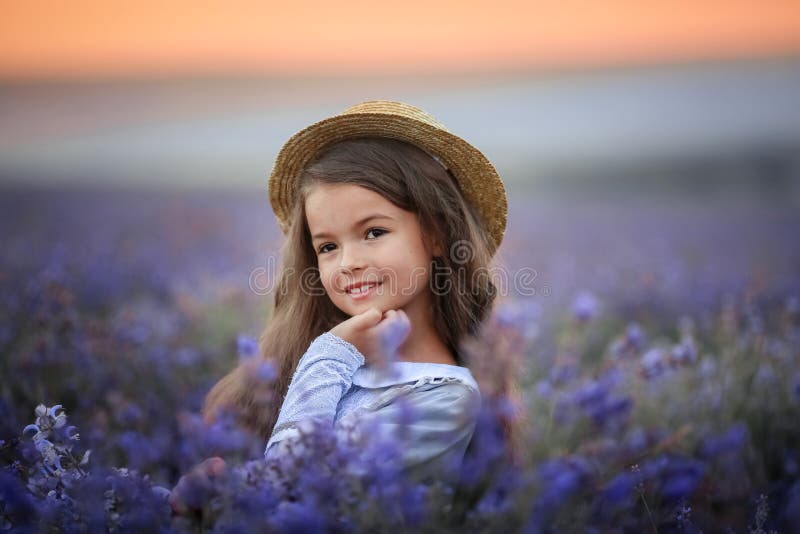 Girl of 8 years dressed in purple cotton dress collects lavender flowers in natural field