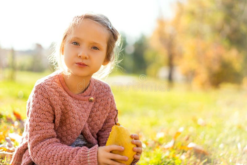Girl 4 years old walks in autumn park holding a pear stock photo Girl 4 years old walks in autumn park holding a pear stock photo