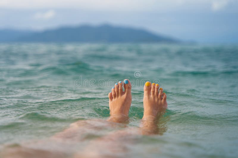 A girl with a yellow and blue pedicure relaxes in the sea overlooking the island