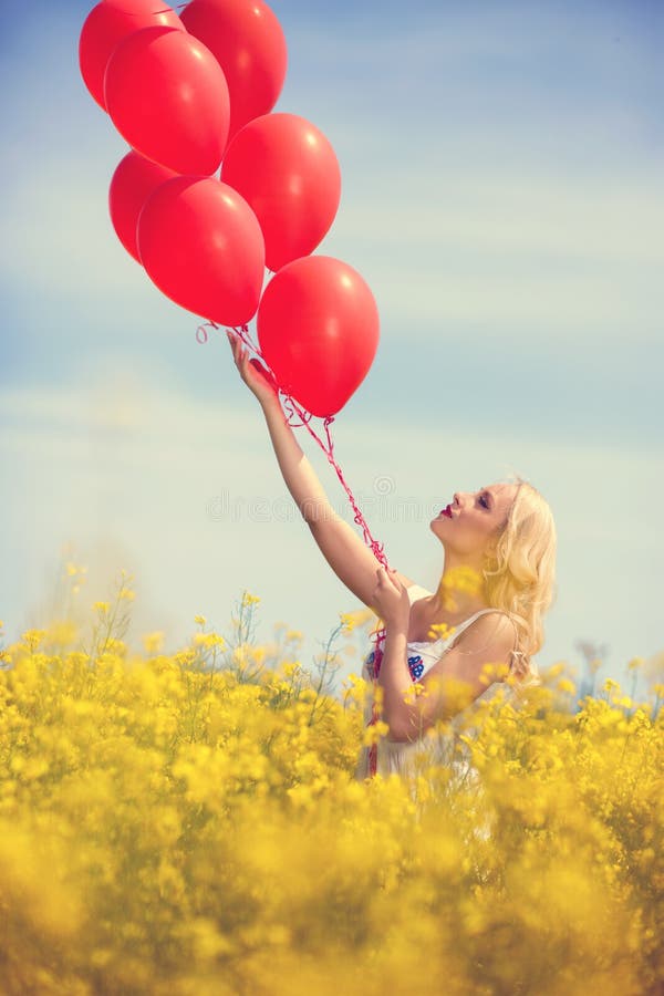 Girl in yellow field letting go of a bunch of balloons