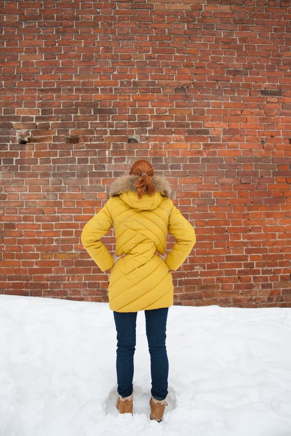 The Girl in the Yellow Jacket Looking at a Brick Wall Stock Photo