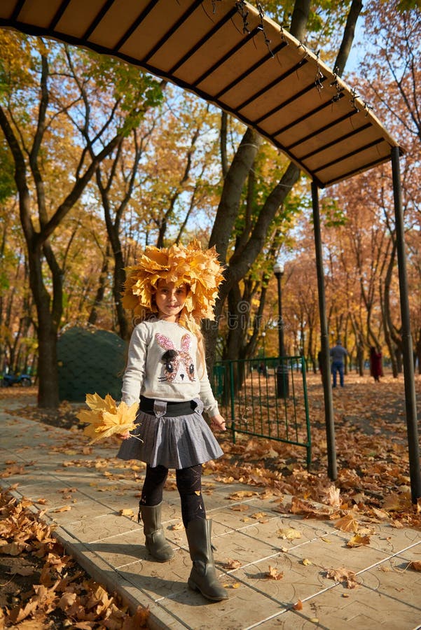 Girl with yellow leaves on her head is in autumn city park. Bright yellow leaves and trees. Happy day.