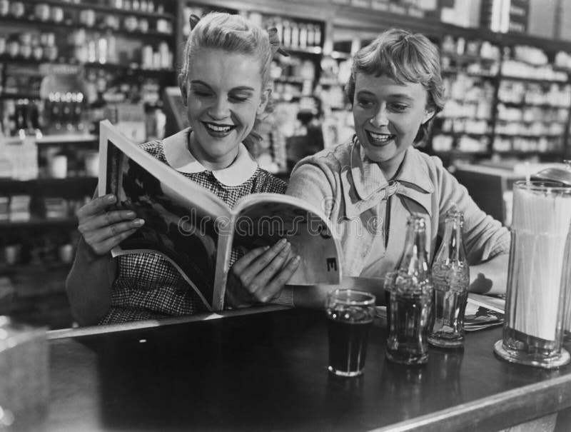 Girlfriends looking at magazine at soda fountain