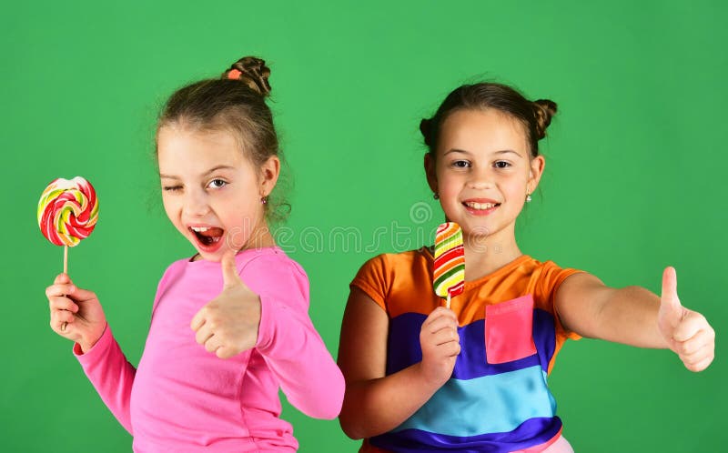 Girls with flirty faces pose with candies on green background.