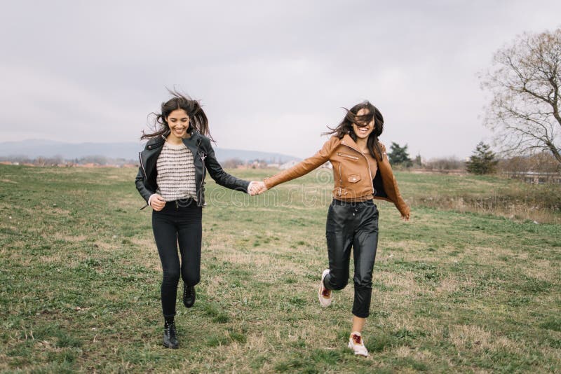 Girls running towards camera and holding hands. Two girls in fashion clothes holding their hands and running outdoors during spring.