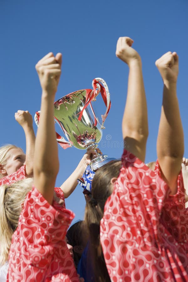 Low angle side view of happy girls soccer team with trophy against clear blue sky. Low angle side view of happy girls soccer team with trophy against clear blue sky