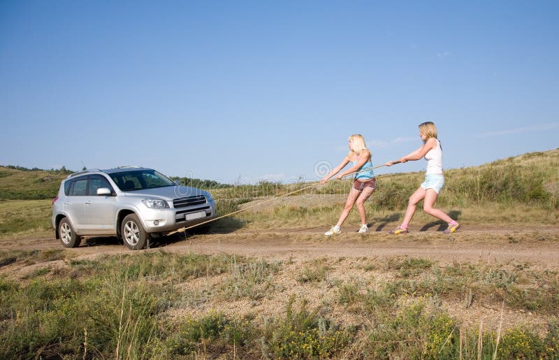 Two young beauty girl tugging car on the solitary road. Two young beauty girl tugging car on the solitary road