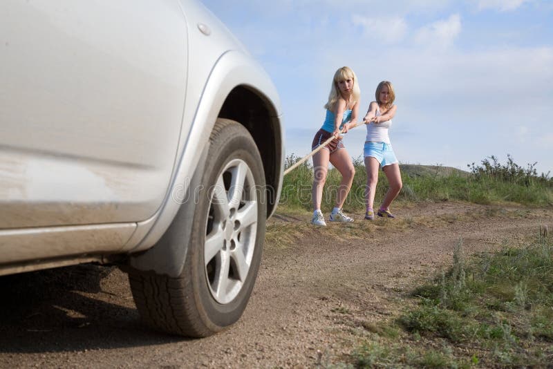 Two young beauty girl tugging car on the solitary road. Two young beauty girl tugging car on the solitary road