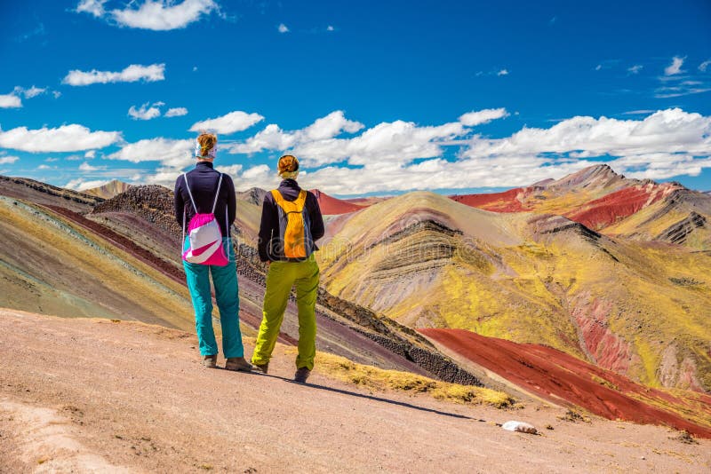Girls watching stunning view at Palccoyo rainbow mountain Vinicunca alternative, mineral colorful stripes in Andean valley