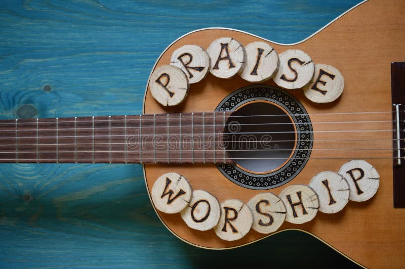 Guitar on teal wooden background with wood pieces on it lettering the words: PRAISE and WORSHIP. Guitar on teal wooden background with wood pieces on it lettering the words: PRAISE and WORSHIP