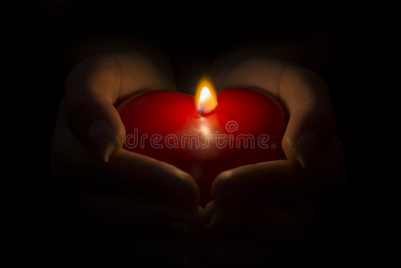 Woman&#x27;s hands holding a heart shaped candle in the dark.