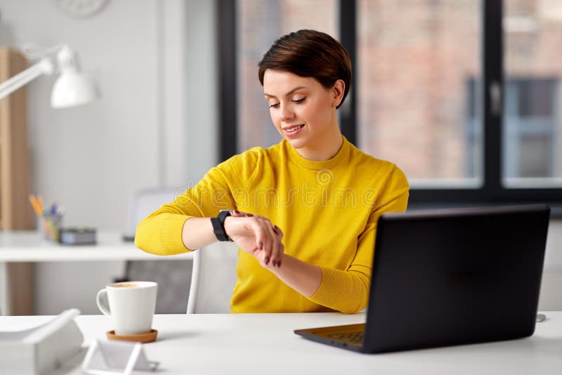 Gl?ckliche Gesch?ftsfrau, die intelligente Uhr im B?ro verwendet lizenzfreie stockfotografie Gl?ckliche Gesch?ftsfrau, die intelligente Uhr im B?ro verwendet lizenzfreie stockfotografie