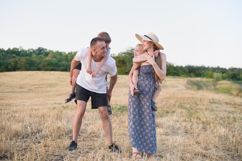 Gl?ckliche junge Familie Ein Vater, eine schwangere Mutter und zwei wenige S?hne auf ihren R?ckseiten Abgeschr?gtes Weizenfeld au lizenzfreie stockfotos Gl?ckliche junge Familie Ein Vater, eine schwangere Mutter und zwei wenige S?hne auf ihren R?ckseiten Abgeschr?gtes Weizenfeld au lizenzfreie stockfotos