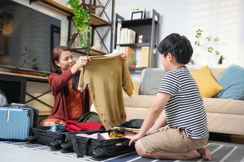 Glad asiatisk familj - Klar för resor till hemmabildskläder till resande moder och son-familjen. arkivfoto