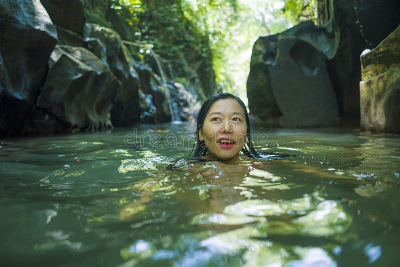 Young beautiful and happy Asian Chinese woman in bikini enjoying unique Summer holidays at tropical forest refreshing relaxed in natural pool delighted by nature beauty swimming at jungle lake. Young beautiful and happy Asian Chinese woman in bikini enjoying unique Summer holidays at tropical forest refreshing relaxed in natural pool delighted by nature beauty swimming at jungle lake