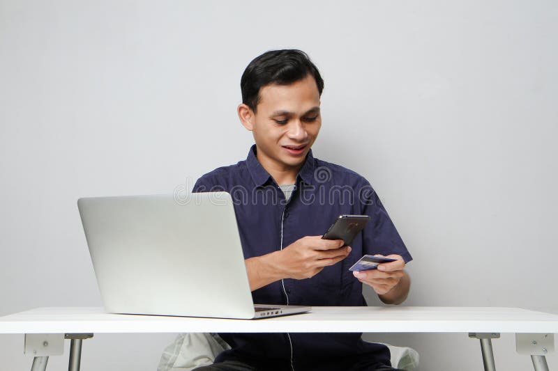 Glad att ha mobiltelefon- och kreditkort medan du sitter framför datorn. på isolerad bakgrund royaltyfria bilder