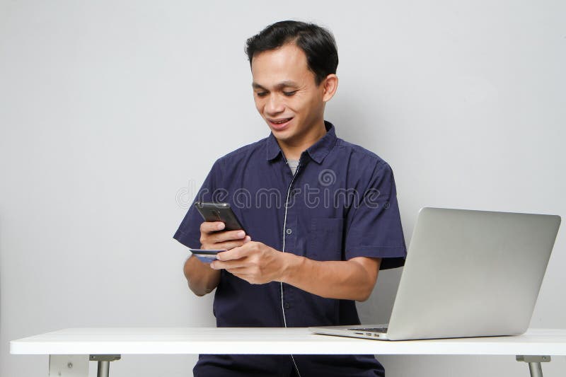 Glad att ha mobiltelefon- och kreditkort medan du sitter framför datorn. på isolerad bakgrund royaltyfri fotografi