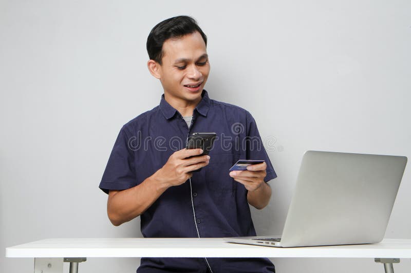 Glad att ha mobiltelefon- och kreditkort medan du sitter framför datorn. på isolerad bakgrund arkivbild