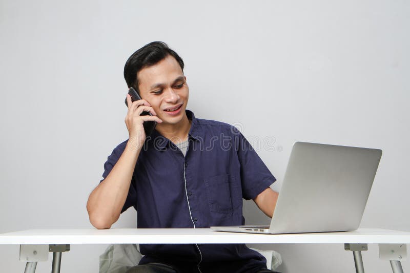 Glad att han ringer ett telefonsamtal medan han sitter framför datorn. på isolerad bakgrund royaltyfri fotografi