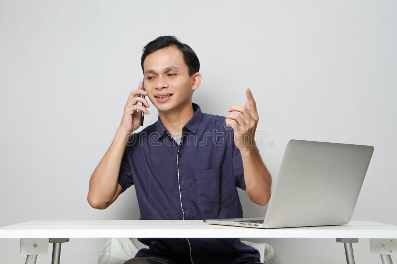 Glad att han ringer ett telefonsamtal medan han sitter framför datorn. på isolerad bakgrund arkivbilder