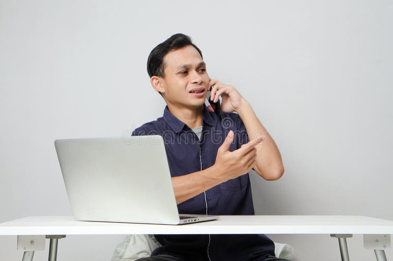 Glad att han ringer ett telefonsamtal medan han sitter framför datorn. på isolerad bakgrund royaltyfri foto