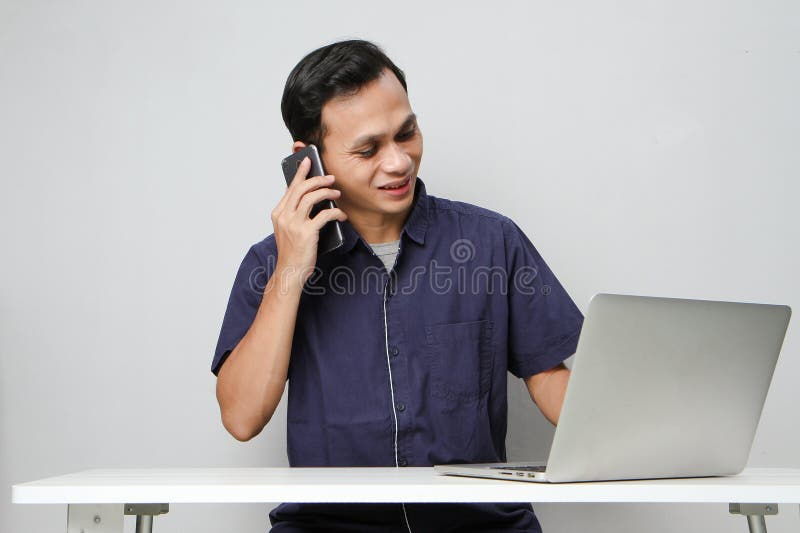 Glad att han ringer ett telefonsamtal medan han sitter framför datorn. på isolerad bakgrund royaltyfri bild