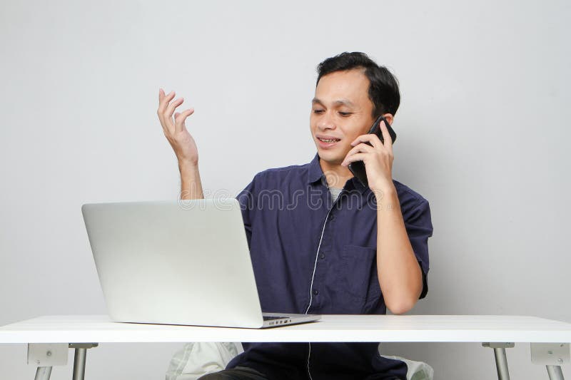 Glad att han ringer ett telefonsamtal medan han sitter framför datorn. på isolerad bakgrund royaltyfri foto