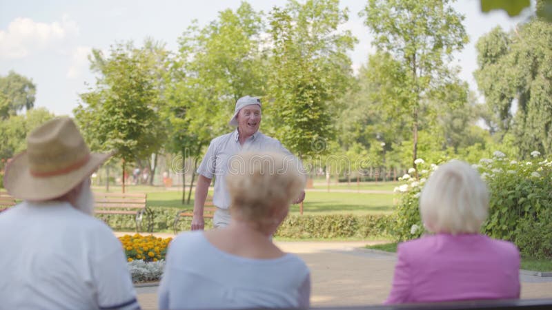 Glad caucasisk pensionär som dansar framför sina vänner som sitter i bänken Positiv gammal kille som roar sig mogen