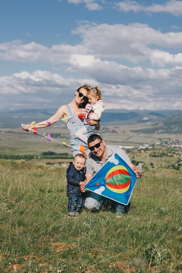 Glad familj som flyger en färglös drake på gröna ängar arkivfoto Glad familj som flyger en färglös drake på gröna ängar arkivfoto