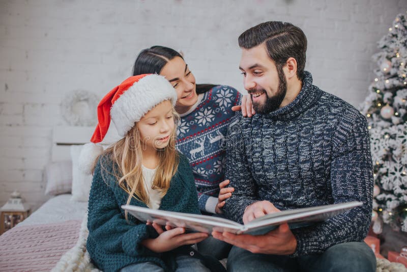 Glad jul och lyckliga ferier gladlynt mamma, farsa och hennes gulliga dotterflicka som läser en bok Förälder och litet barn royaltyfri fotografi