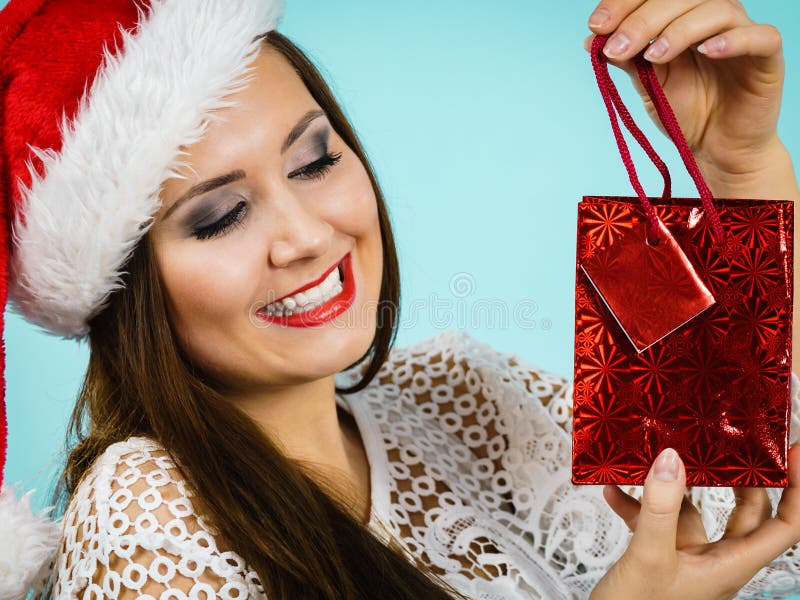 Glad jultomtkvinna har presentsäck. Den unga vuxna kvinnan ger gärna julklappar. Kvinnor som bär jultomtehatt som håller i en röd presentväska i blått