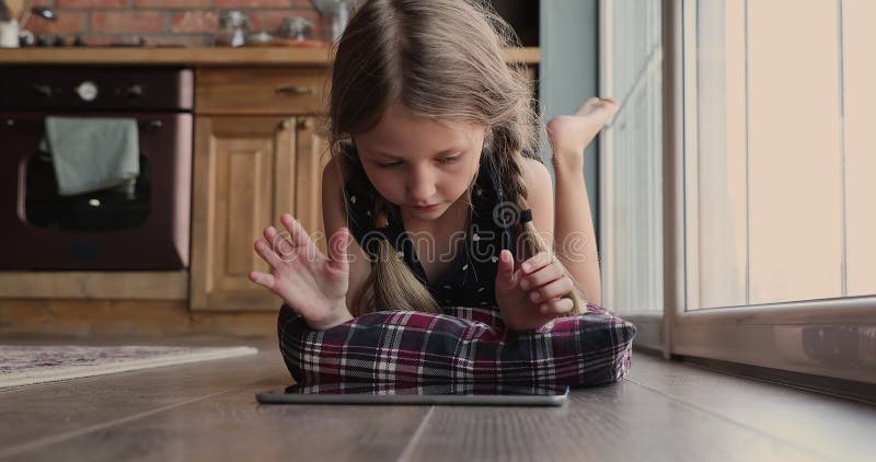 Glad liten söt flicka som använder en datortablett som ligger på golvet.