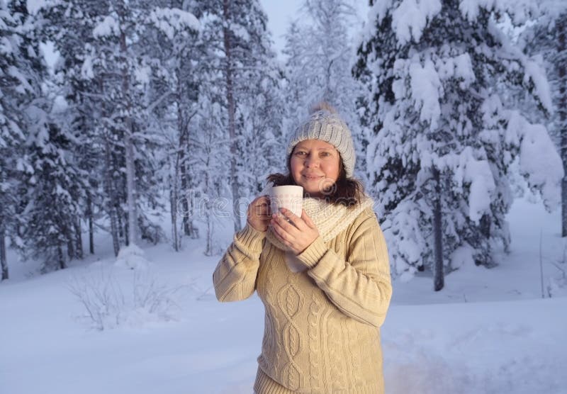 Happy mature woman 50 years old drink hot tea in winter forest, early evening in park among snow-covered trees, beautiful landscape, smiling happily, concept active lifestyle, enjoying winter nature. Happy mature woman 50 years old drink hot tea in winter forest, early evening in park among snow-covered trees, beautiful landscape, smiling happily, concept active lifestyle, enjoying winter nature