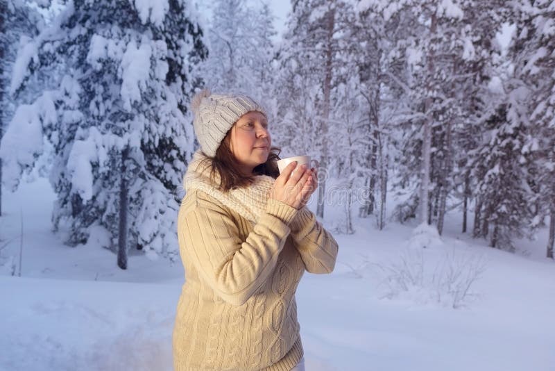 happy mature woman 50 years old drink hot tea in winter forest, early evening in park among snow-covered trees, beautiful landscape, smiling happily, concept active lifestyle, enjoying winter nature. happy mature woman 50 years old drink hot tea in winter forest, early evening in park among snow-covered trees, beautiful landscape, smiling happily, concept active lifestyle, enjoying winter nature