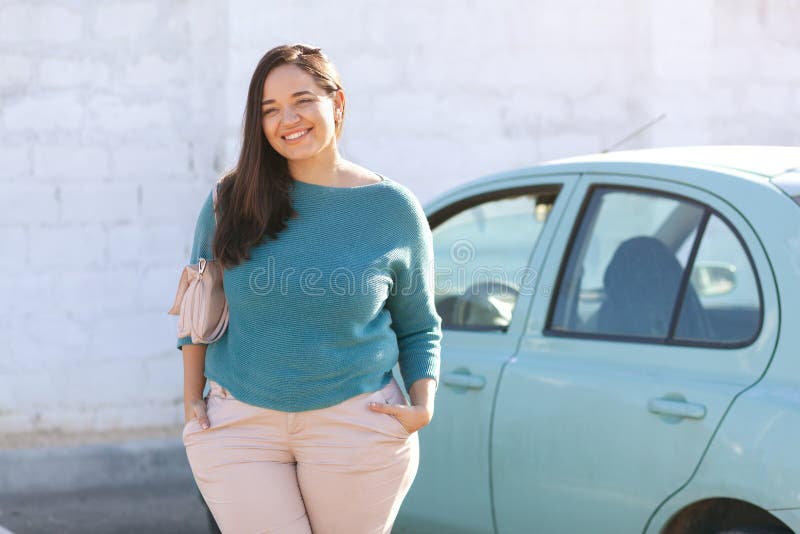 Outdoor portrait of happy beautiful plus size woman driver wearing casual clothes posing outside of the blue rental car in sunny day. Outdoor portrait of happy beautiful plus size woman driver wearing casual clothes posing outside of the blue rental car in sunny day