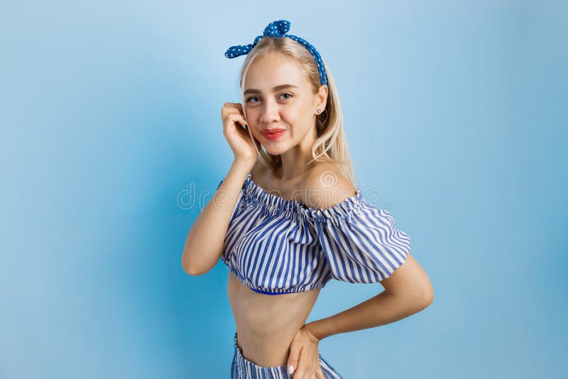 Glad och upphetsad härlig blond flicka i sommardräkt och att posera på kameran som står över blå bakgrund arkivbild Glad och upphetsad härlig blond flicka i sommardräkt och att posera på kameran som står över blå bakgrund arkivbild