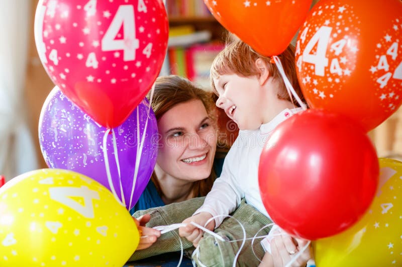 Glad pojke och mor som firar sin 4-årsdag med färgfulla ballonger. Barn och unga kvinnor som kramar royaltyfria foton