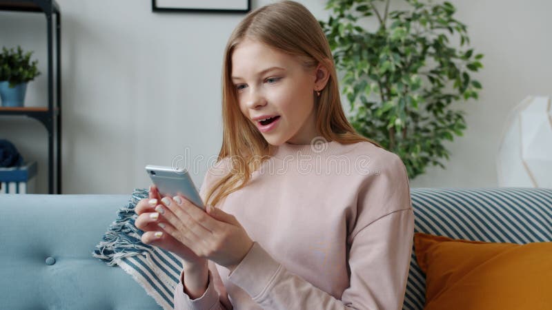 Glad tonåring som får goda nyheter med smartphone som uttrycker positiva känslor hemma