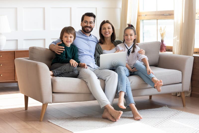 Glad ung familj sitter på soffan med modern bärbar dator arkivfoton