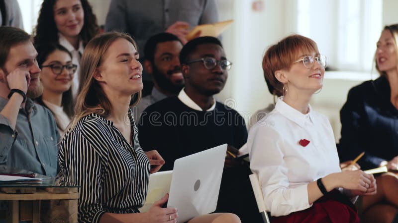 Glad ung företagspartner med flera etniska grupper diskuterar seminarier med talare, leende och skratt vid det moderna mötet på l