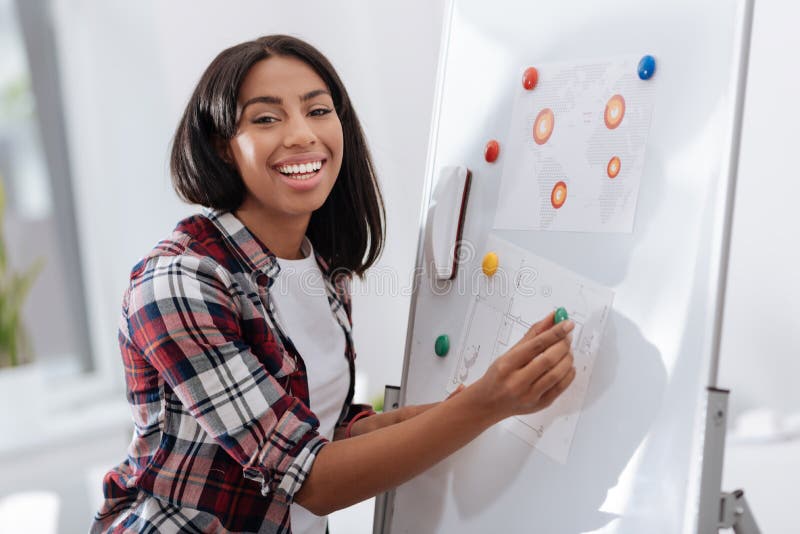 Glad ung kvinna som sätter visuella material på whiteboarden royaltyfri bild Glad ung kvinna som sätter visuella material på whiteboarden royaltyfri bild