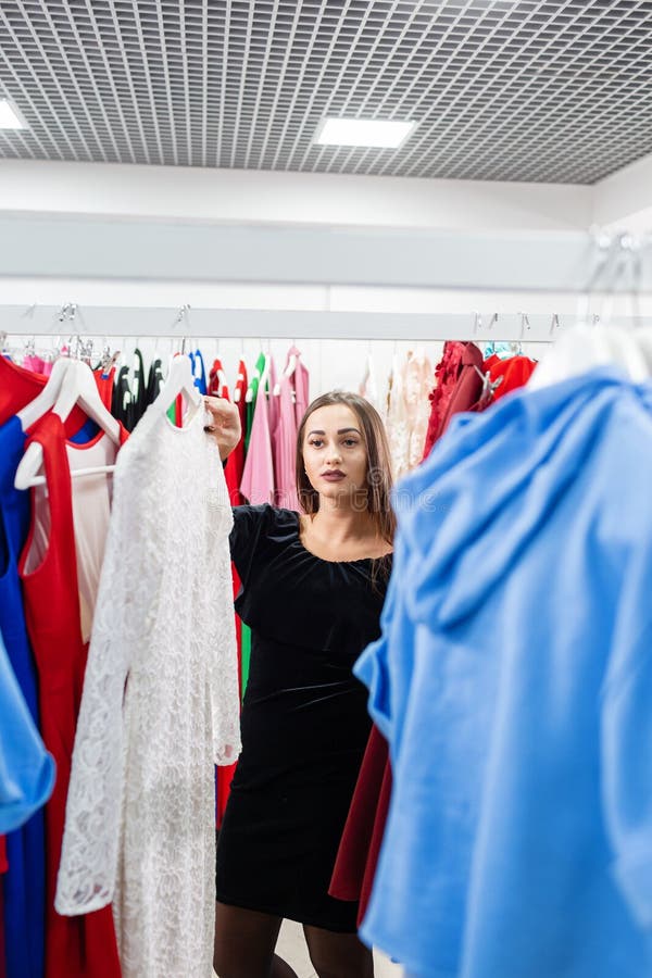 Glad ung kvinna som väljer kläder i köpcentra eller i klädesplagg Försäljning, mode, konsumtionskoncept royaltyfria bilder