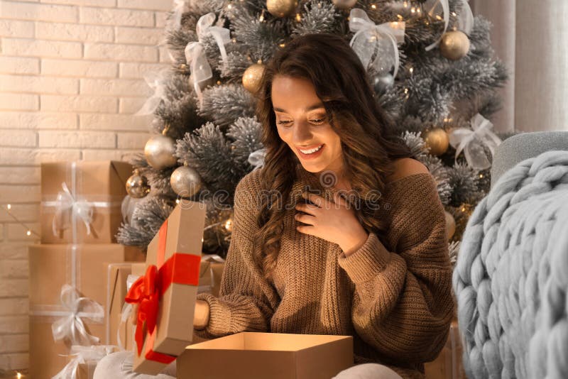Glad ung kvinna som öppnar julklapp hemma Magisk semester arkivbild