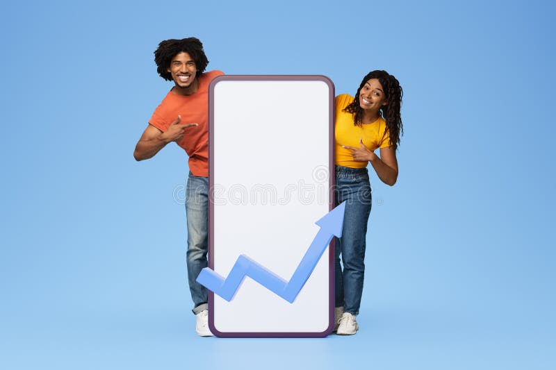 Glad young black couple pointing fingers at large phone with blank screen with abstract graph stock images