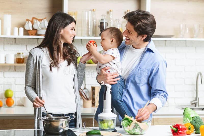 Glada föräldrar som förbereder lunch med babyson i köket arkivbild