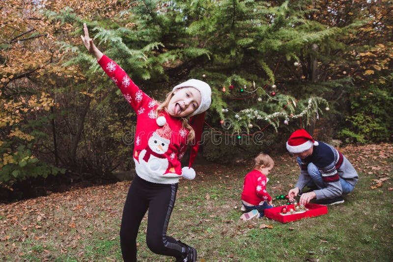 glada lyckliga ferier för jul Den nätta flickan i röd tröja och julhatt har gyckel, och hennes familj dekorerar en jultre royaltyfria foton glada lyckliga ferier för jul Den nätta flickan i röd tröja och julhatt har gyckel, och hennes familj dekorerar en jultre royaltyfria foton