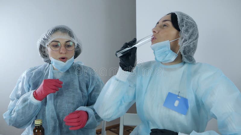 Glada läkare har kul i laboratoriet. Vetenskapliga kvinnliga läkare i en blå rock dricker vätska från en glasflaska i stock video