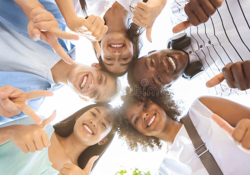 International Friendship. Group Of Joyful Multicultural Teenagers Standing In Circle, Showing Funny Gestures, Posing At Camera Outdoors, Low Angle. International Friendship. Group Of Joyful Multicultural Teenagers Standing In Circle, Showing Funny Gestures, Posing At Camera Outdoors, Low Angle