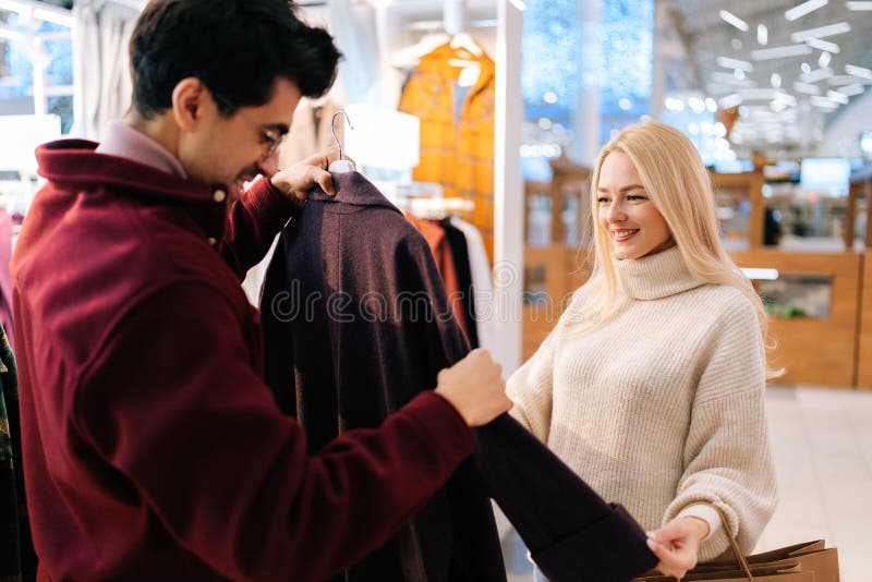 Glada, glada, unga par som väljer modekvinnlig rock tillsammans i klädesbutiken på shoppingcentret. blond kvinna arkivbilder